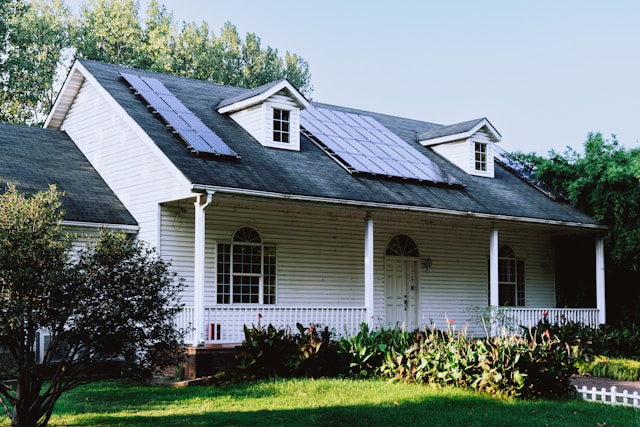 Small white house with a black roof surrounded by trees, showcasing a cozy residential property suitable for solar panel installation in Minnesota.