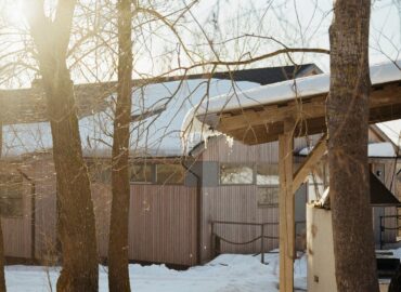 maria-karelskaya-CelZhNiVKjQ-unsplash A snow-covered house nestled in a snowy forest clearing under a grey winter sky