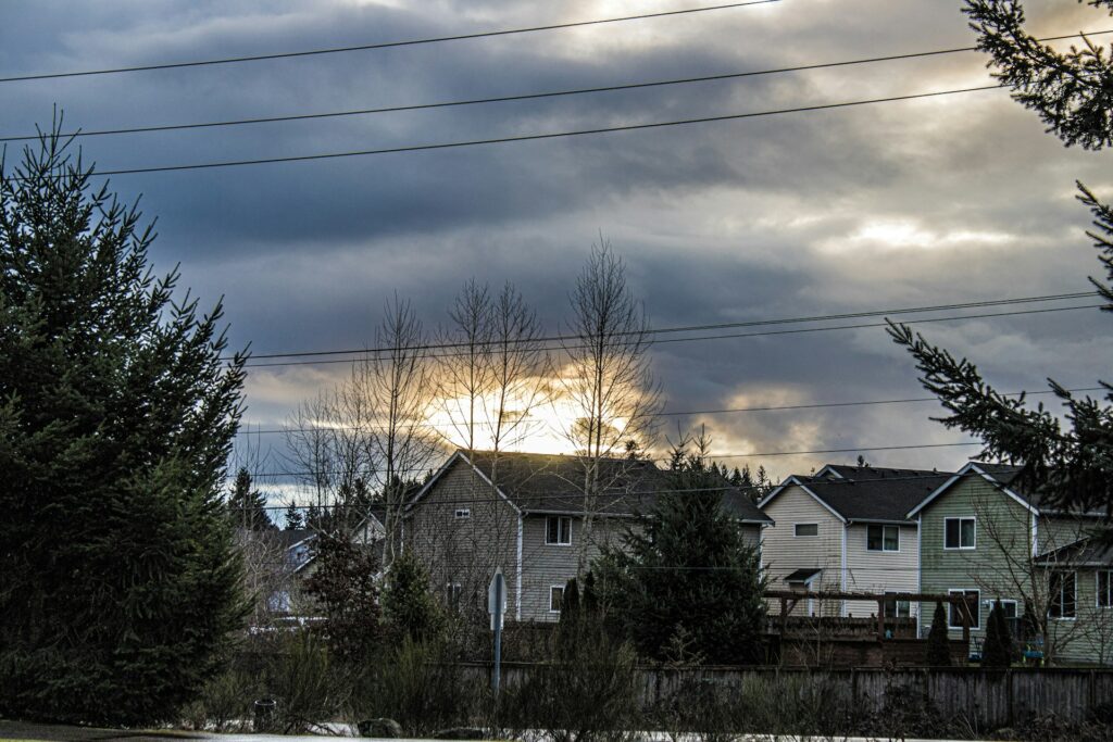 Sunlight breaking through clouds over suburban houses in Minnesota, illustrating how solar panels can still generate energy on cloudy days.