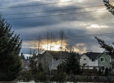 Sunlight breaking through clouds over suburban houses in Minnesota, illustrating how solar panels can still generate energy on cloudy days.