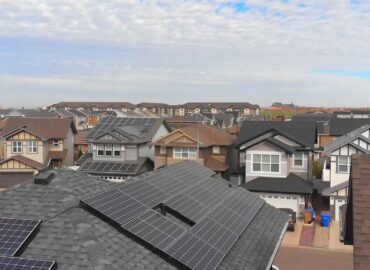 Row of modern houses with solar panels installed on their roofs under clear blue sky, showcasing sustainable residential energy solutions.