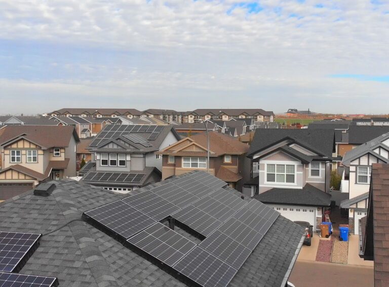 scott-goodwill-hKUJRPAAFWo-unsplash Row of modern houses with solar panels installed on their roofs under clear blue sky, showcasing sustainable residential energy solutions.