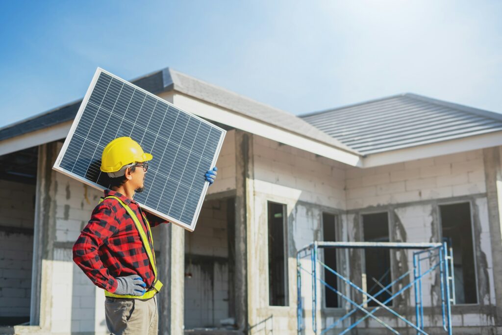 A man holding a solar panel in front of a house, representing residential solar energy installation and sustainable power solutions in Saint Paul.